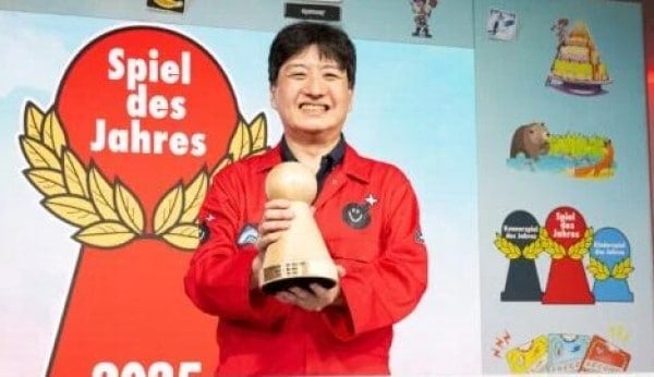 A man in a red shirt smiling whole holding up a trophy.